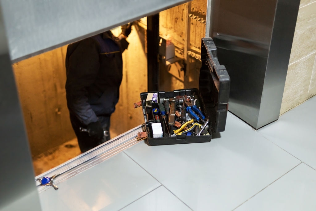 Specialist fixing or adjusting lift mechanism in elevator schaft. Regular repair, service and maintenance of elevator.